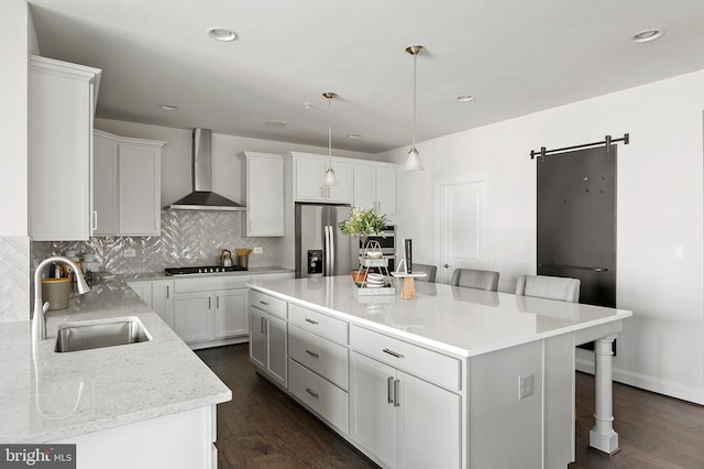 kitchen featuring wall chimney exhaust hood, sink, a center island, stainless steel fridge with ice dispenser, and a barn door