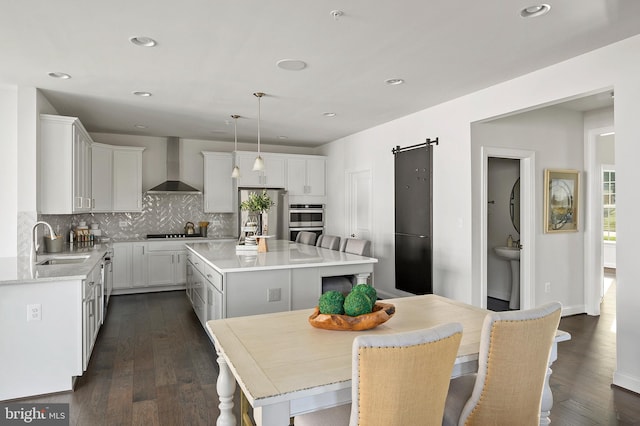 kitchen featuring wall chimney range hood, a kitchen island, a barn door, pendant lighting, and sink