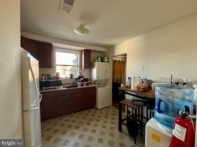 kitchen featuring visible vents, a sink, stainless steel microwave, freestanding refrigerator, and stacked washer / dryer