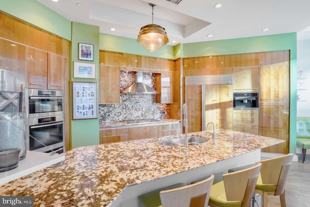 kitchen featuring tasteful backsplash, a kitchen breakfast bar, pendant lighting, wall chimney exhaust hood, and sink