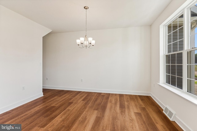 empty room with a notable chandelier and dark hardwood / wood-style flooring