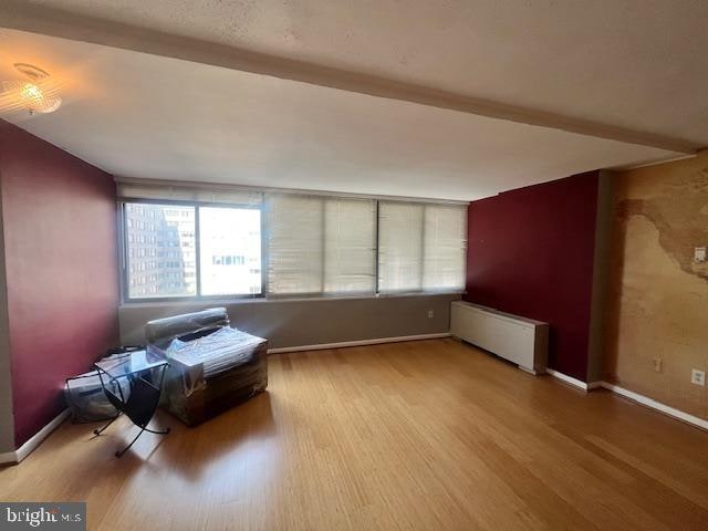 living area with beam ceiling, radiator, and hardwood / wood-style floors