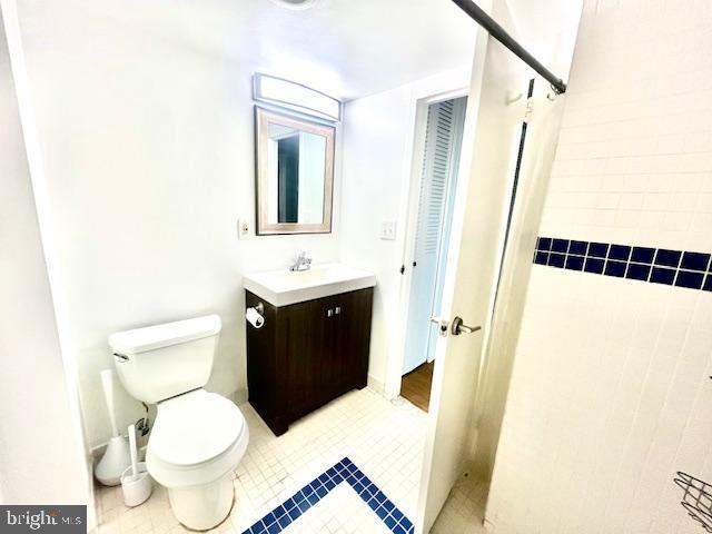 bathroom with tile patterned floors, vanity, tiled shower, and toilet