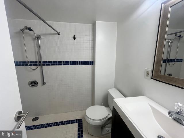 bathroom with tiled shower, tile patterned flooring, vanity, and toilet