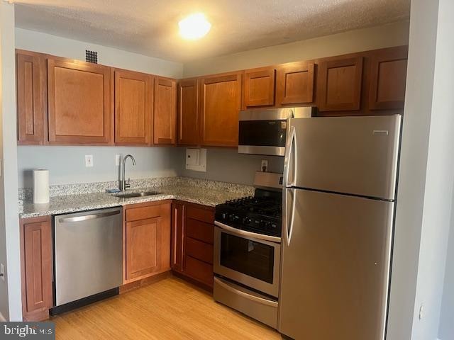 kitchen featuring sink, a textured ceiling, light hardwood / wood-style floors, light stone counters, and stainless steel appliances