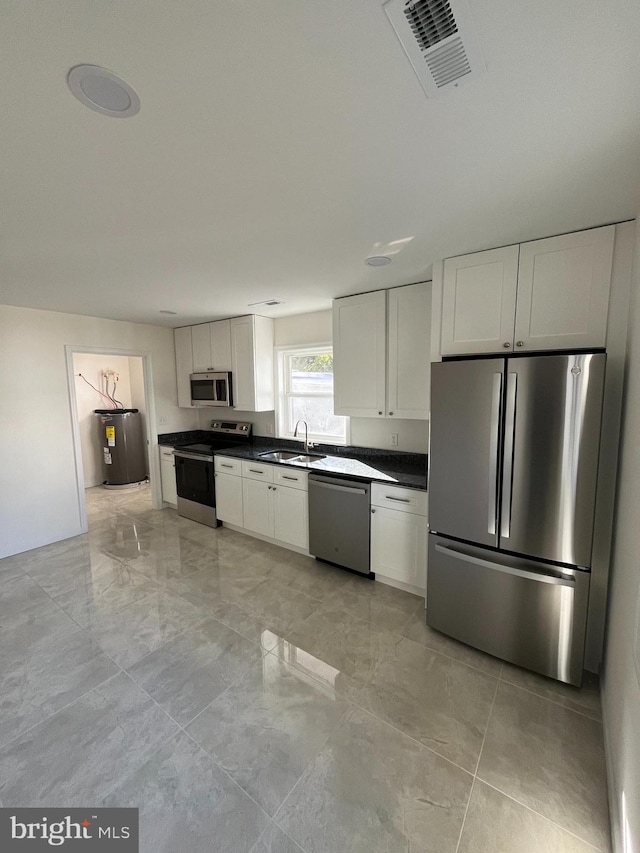 kitchen with appliances with stainless steel finishes, white cabinets, electric water heater, and sink