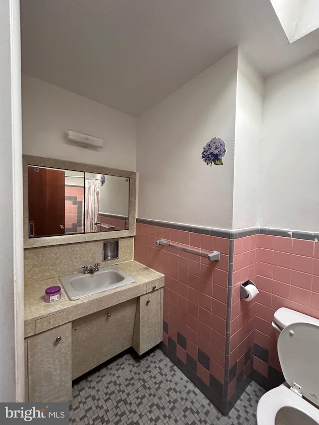 bathroom with tile walls, toilet, a skylight, vanity, and tile patterned floors