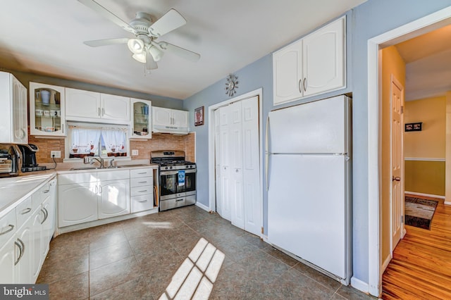 kitchen featuring gas stove, white fridge, backsplash, sink, and white cabinets