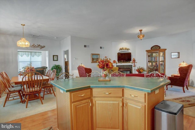 kitchen with light hardwood / wood-style flooring, a center island, a tile fireplace, and decorative light fixtures