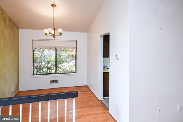 corridor with hardwood / wood-style floors, an inviting chandelier, and lofted ceiling