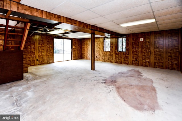 basement featuring a paneled ceiling and wooden walls