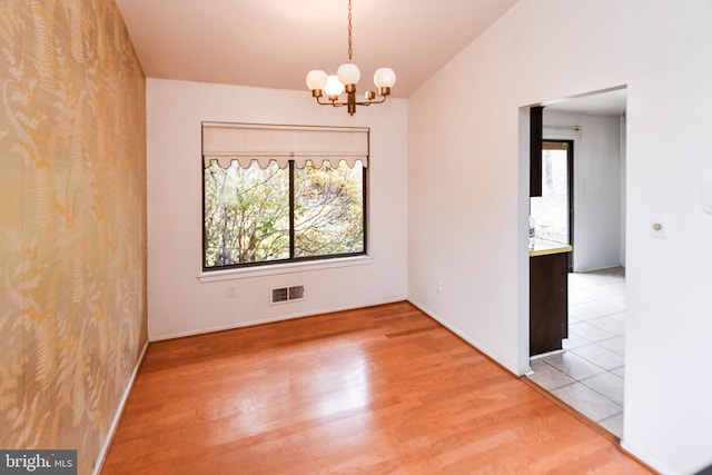 unfurnished room featuring an inviting chandelier, a healthy amount of sunlight, and wood-type flooring