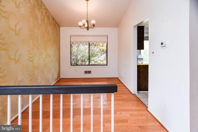 hallway with lofted ceiling, wood-type flooring, and an inviting chandelier