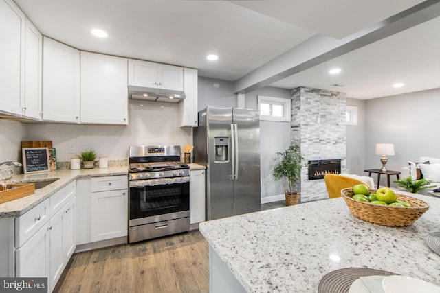 kitchen with appliances with stainless steel finishes, white cabinets, a stone fireplace, and sink