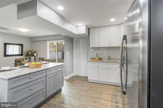 kitchen with sink, stainless steel fridge, light stone countertops, light hardwood / wood-style floors, and tasteful backsplash