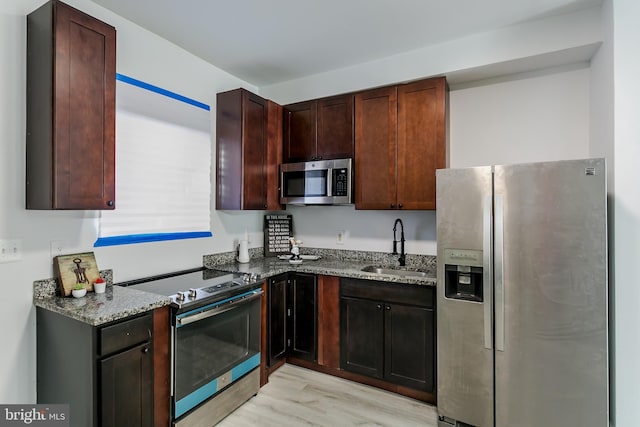 kitchen with sink, stainless steel appliances, light hardwood / wood-style floors, and dark stone countertops