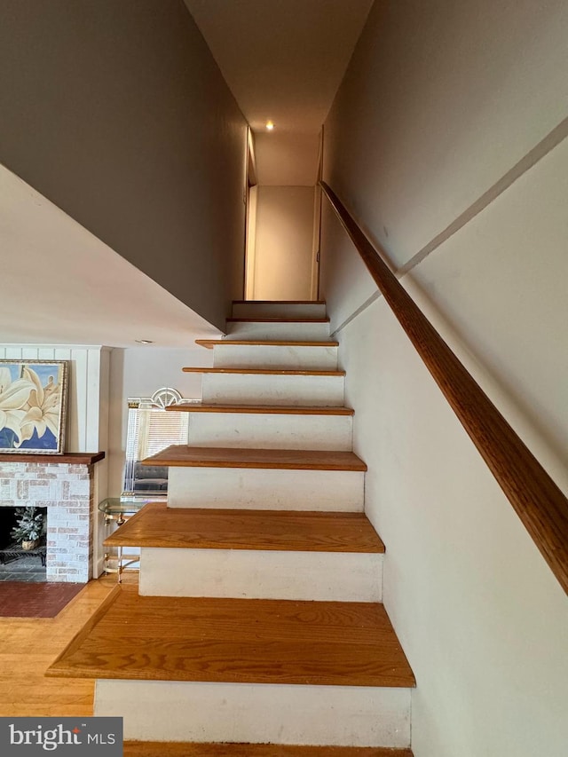 stairs featuring hardwood / wood-style floors and a brick fireplace