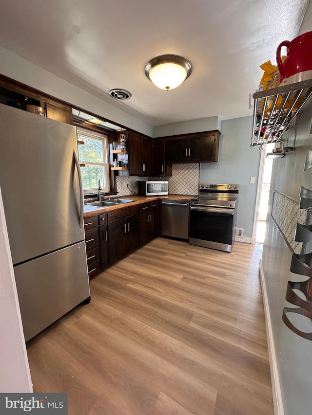 kitchen with sink, stainless steel appliances, dark brown cabinets, and light hardwood / wood-style flooring