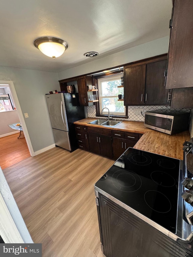 kitchen with decorative backsplash, light wood-type flooring, dark brown cabinets, stainless steel appliances, and sink