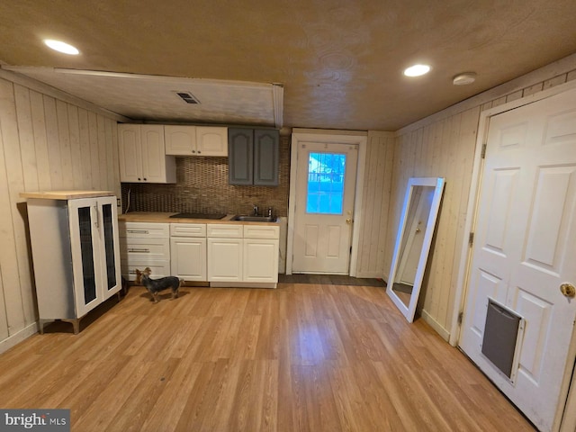 kitchen with backsplash, wood walls, light hardwood / wood-style flooring, and sink