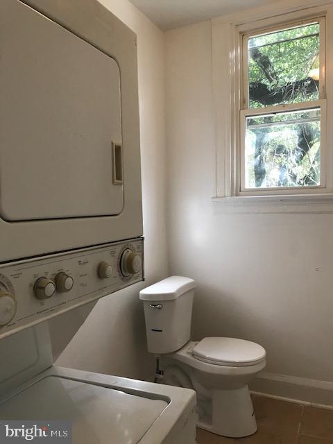 clothes washing area with stacked washing maching and dryer and tile patterned floors