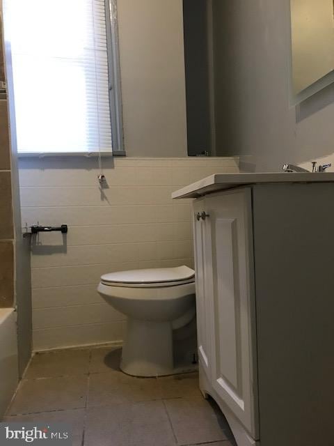 bathroom with toilet, vanity, tile patterned floors, and tile walls