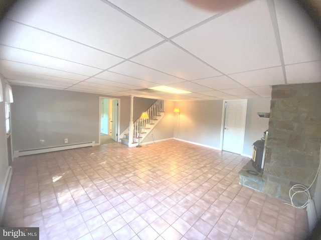 basement with a drop ceiling, a wood stove, and a baseboard radiator