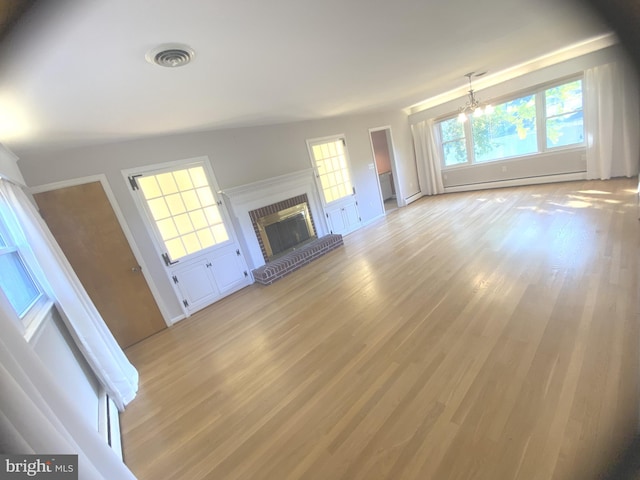 unfurnished living room with light hardwood / wood-style floors, a brick fireplace, baseboard heating, and a chandelier