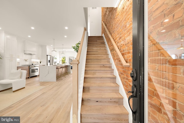 stairs with hardwood / wood-style floors and brick wall