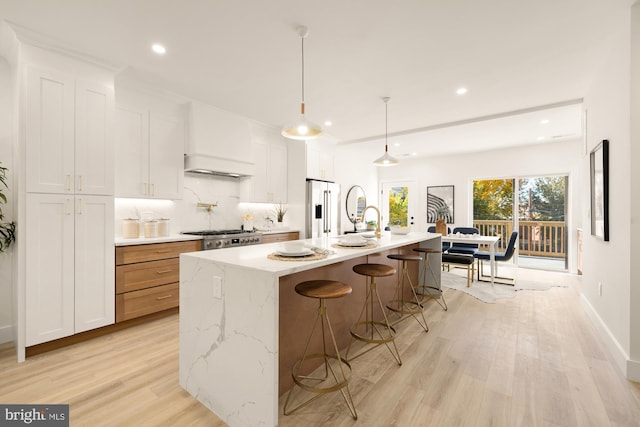 kitchen with light wood-type flooring, stainless steel appliances, decorative light fixtures, white cabinets, and an island with sink