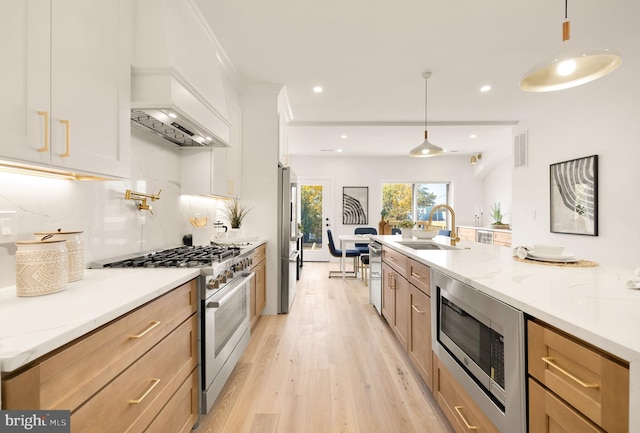 kitchen with light stone countertops, appliances with stainless steel finishes, light wood-type flooring, decorative light fixtures, and white cabinets