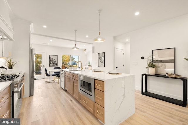 kitchen featuring a large island with sink, light stone countertops, decorative light fixtures, light hardwood / wood-style floors, and stainless steel appliances