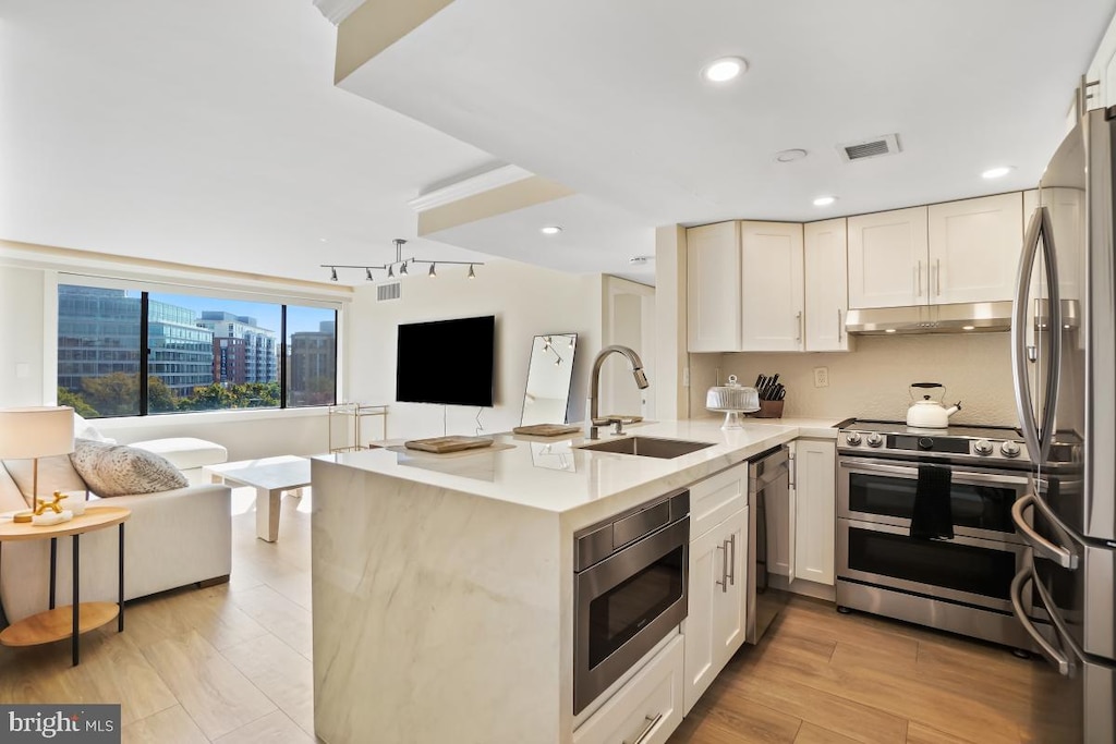 kitchen featuring kitchen peninsula, sink, white cabinetry, appliances with stainless steel finishes, and light hardwood / wood-style floors