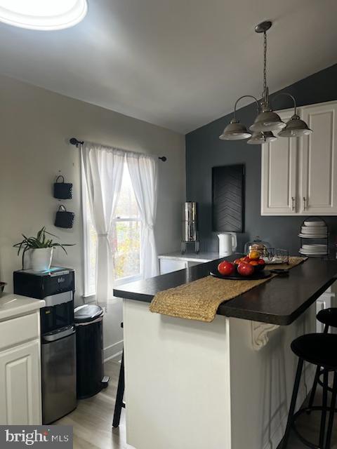 kitchen featuring a kitchen bar, white cabinets, a chandelier, and light wood-type flooring