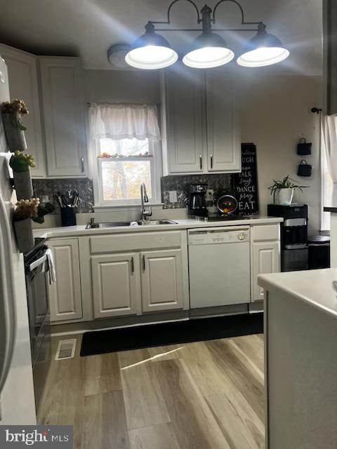 kitchen with white dishwasher, white cabinetry, and sink