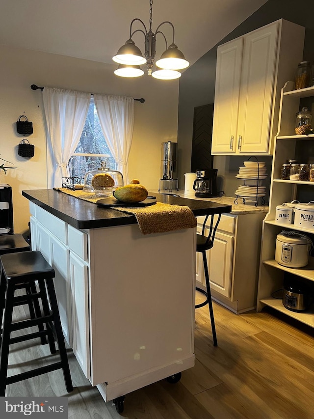 kitchen with a kitchen bar, dark wood-type flooring, decorative light fixtures, an inviting chandelier, and white cabinets