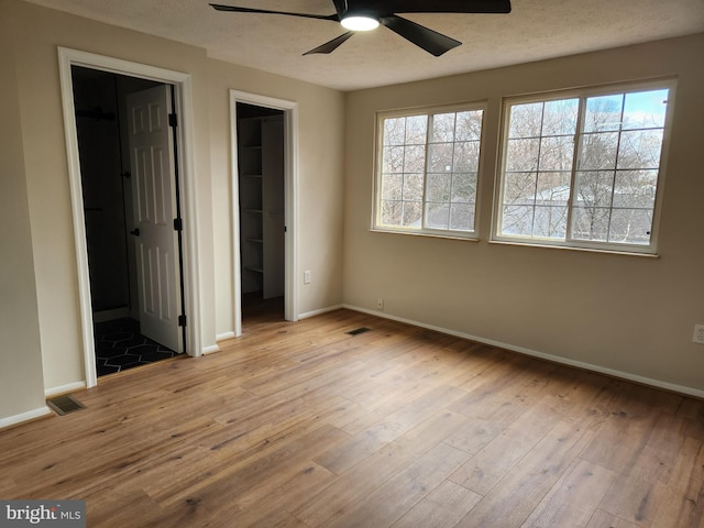 unfurnished bedroom with a walk in closet, ceiling fan, light hardwood / wood-style floors, and multiple windows