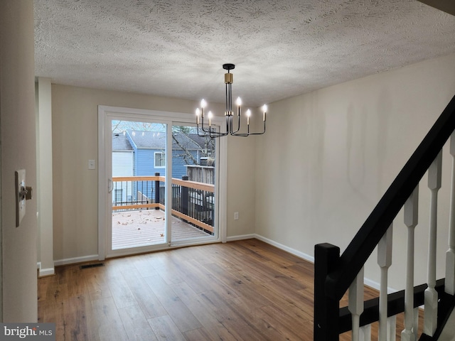 unfurnished dining area featuring a chandelier, wood-type flooring, and a textured ceiling