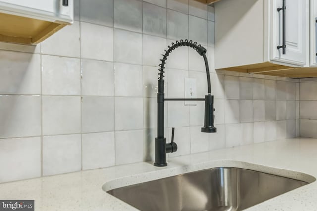 room details featuring white cabinetry, sink, light stone countertops, and backsplash