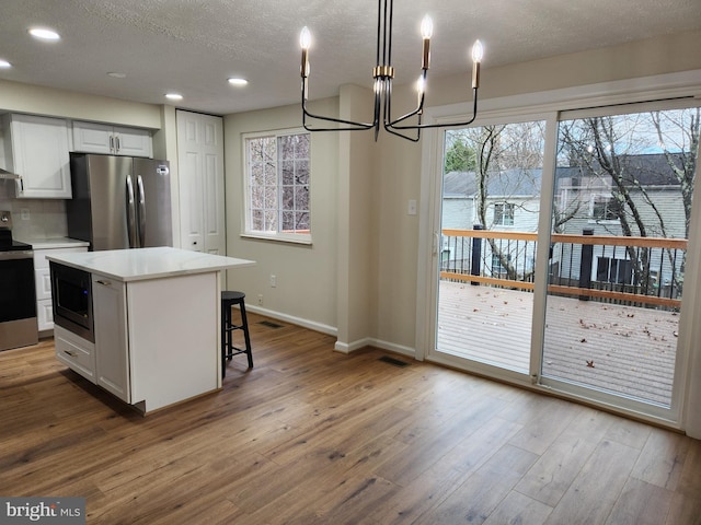 kitchen featuring white cabinetry, a center island, stainless steel appliances, a notable chandelier, and decorative light fixtures