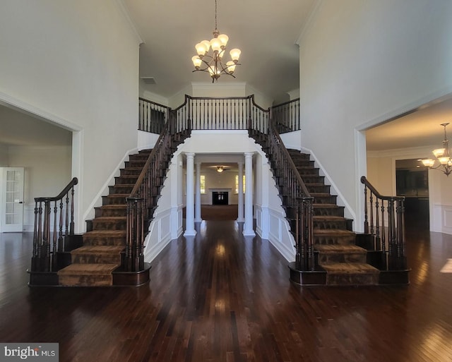 entrance foyer featuring decorative columns, crown molding, a towering ceiling, and dark hardwood / wood-style flooring