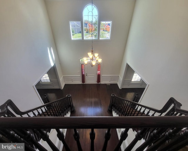 stairs featuring a notable chandelier, hardwood / wood-style flooring, and a towering ceiling