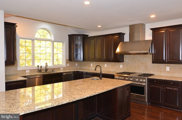 kitchen with wall chimney range hood, sink, dark brown cabinets, stainless steel appliances, and dark hardwood / wood-style floors