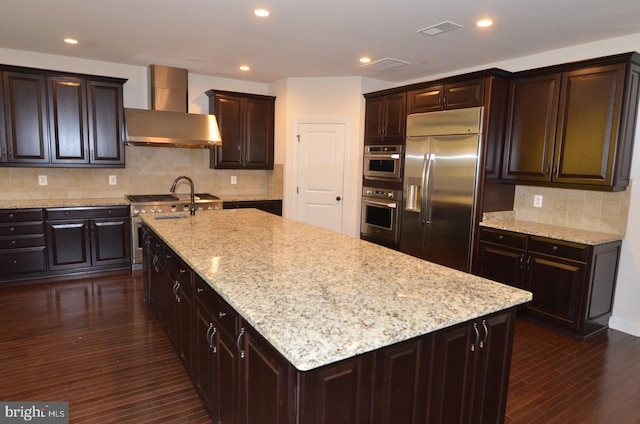 kitchen featuring backsplash, wall chimney exhaust hood, appliances with stainless steel finishes, and dark hardwood / wood-style flooring