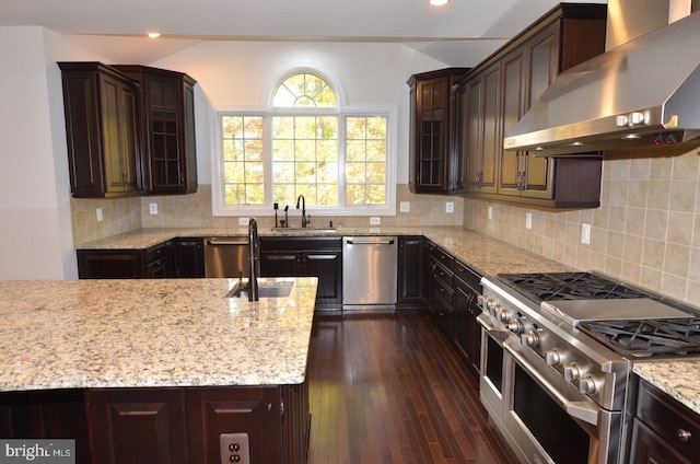 kitchen with wall chimney range hood, dark wood-type flooring, sink, dark brown cabinetry, and stainless steel appliances