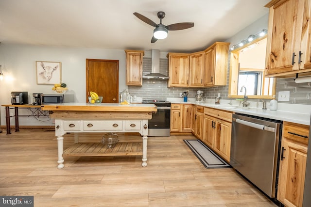 kitchen featuring light hardwood / wood-style floors, stainless steel appliances, wall chimney exhaust hood, and ceiling fan