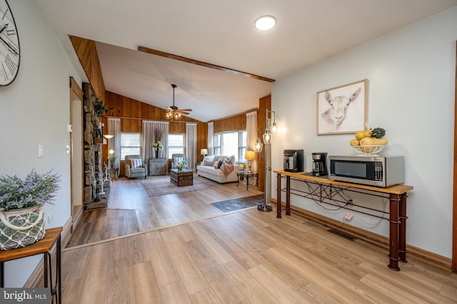 living room with ceiling fan, wood walls, vaulted ceiling, and light wood-type flooring