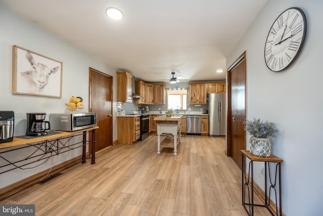 kitchen with decorative backsplash, a kitchen island, appliances with stainless steel finishes, ceiling fan, and light wood-type flooring