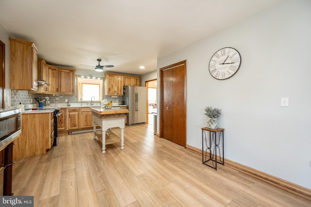 kitchen featuring backsplash, sink, appliances with stainless steel finishes, light hardwood / wood-style floors, and ceiling fan