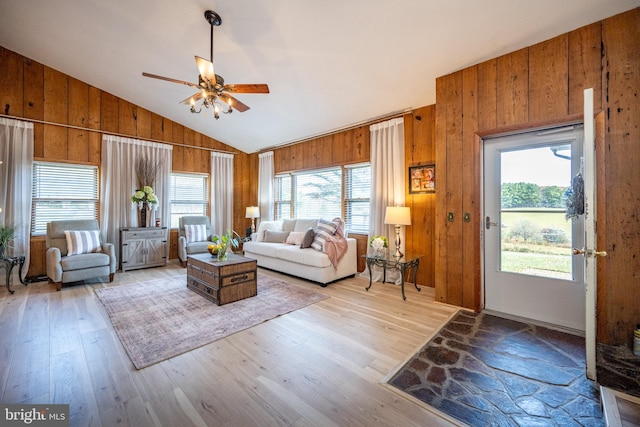 living room with ceiling fan, wood walls, lofted ceiling, and light wood-type flooring